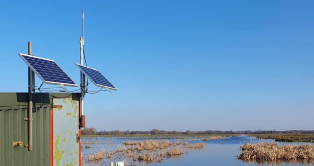 two solar panels mounted on building with wetland and blue sky